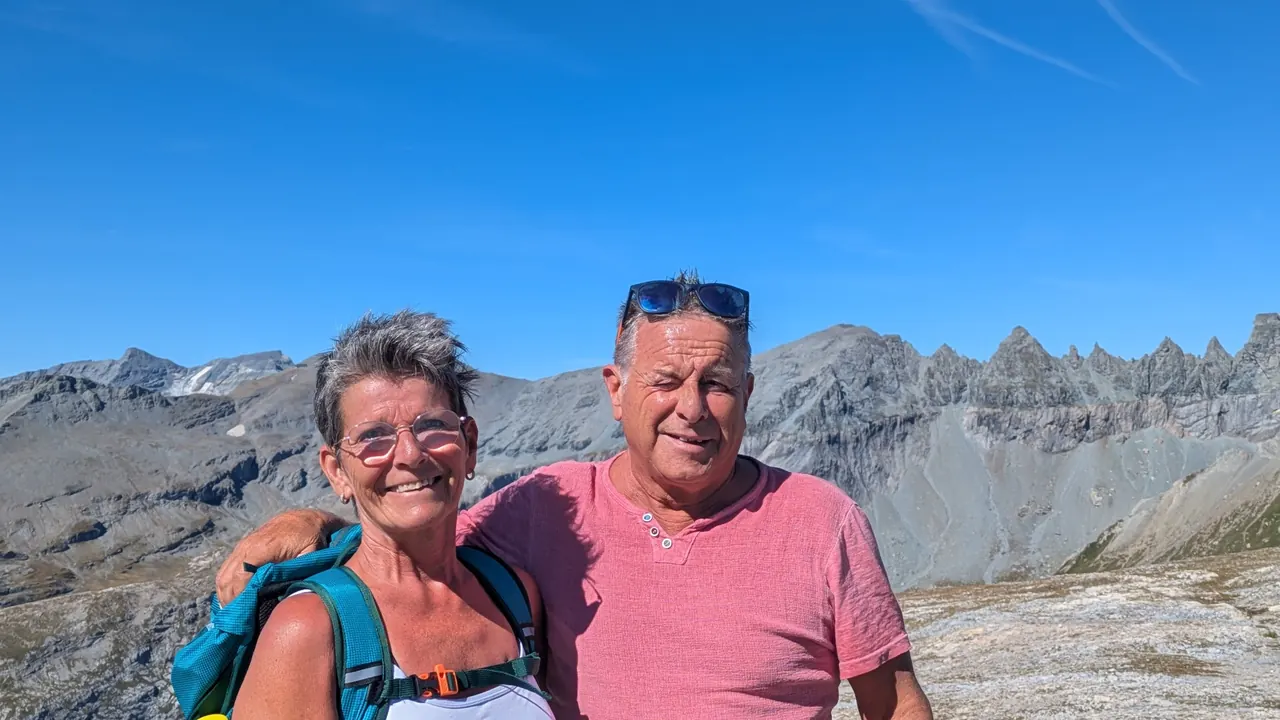 Corina und Donat nebeneinander in den Bergen, dahinter Felsgipfel und blauer Himmel
