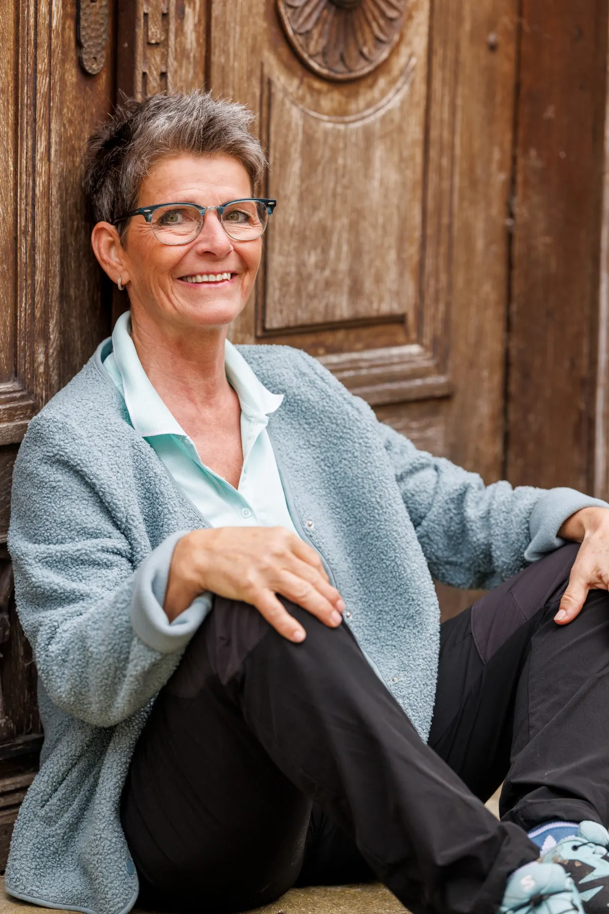 Portrait von Corina, sitzend vor einer alten Holztür, lächelnd